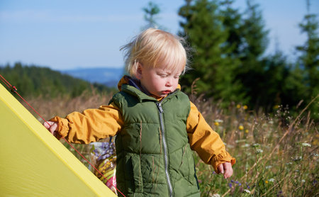 Curious kid looking for something in grass. Cute toddler standing next to yellow tent on background of forest.の写真素材