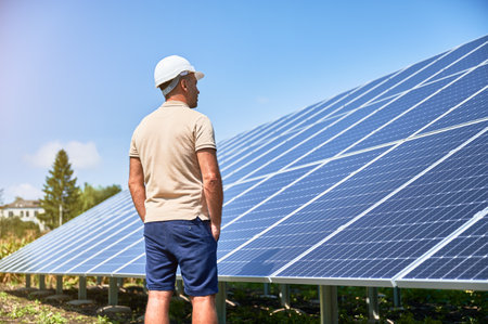 Back view of man in helmet next to solar system. Confident man looking at his investment. Male adult looking at photovoltaic batteries.の写真素材