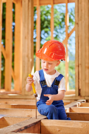 Young boy indulges in playful construction of timber-framed house. Toddler acquiring skill of extracting driven nail with hammer. Concept of early childhood development and parental assistance.の写真素材