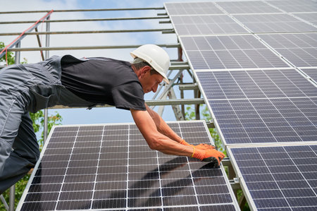 Cropped view of man engineer solar installer placing solar module on metal rails. Male worker installing photovoltaic solar panel system. Concept of alternative energy and power sustainable resources.の写真素材