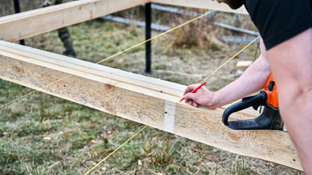 Man worker building wooden frame house on pile foundation. Close up carpenter measuring wooden planks and making marks with pencil. Carpentry concept.の写真素材