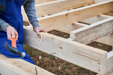 Man worker building wooden frame house on pile foundation. Carpenter hammering nail into wooden joist, using hammer. Carpentry concept.の写真素材