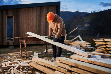 Man worker building wooden frame house. Carpenter using tape measure for measuring wooden planks and making marks with pencil. Carpentry concept.の写真素材