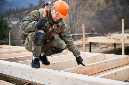 Man worker building wooden frame house on pile foundation. Carpenter hammering nail into wooden plank, using hammer. Carpentry concept.の写真素材