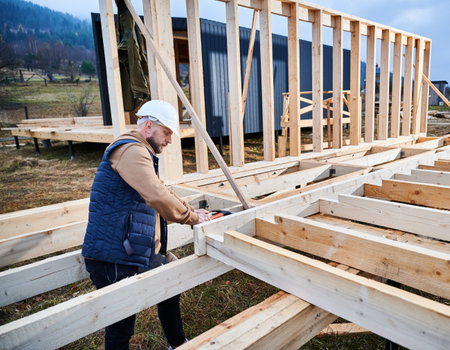 Man worker building wooden frame house on pile foundation. Carpenter hammering nail into wooden truss, using hammer. Carpentry concept.の写真素材