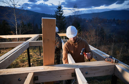 Men workers building wooden frame house on pile foundation. Carpenters installing wooden board for timber framing, using hammers. Carpentry concept.の写真素材