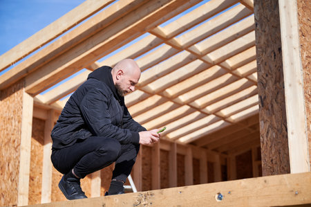 Male inspector building wooden frame house. Bald man standing on construction site, inspecting quality of work on sunny day.の写真素材