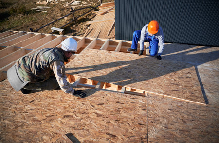 Carpenters mounting wooden OSB board on rooftop of future cottage. Men workers building wooden frame house. Carpentry and construction concept.の写真素材