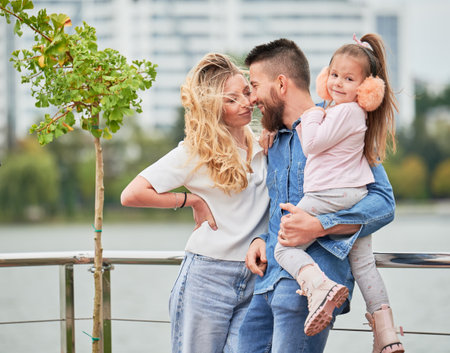 Man and woman with child outdoors. Father holding adorable child while spending time with family in new urban district.の写真素材