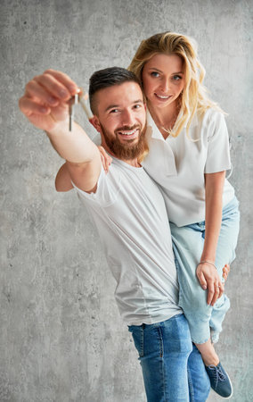 Cheerful man holding wife and smiling while showing apartment keys. Happy couple real estate house buyers demonstrating keys from new home.の写真素材