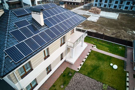 Residential house with photovoltaic solar panel modules on rooftop and green grass on backyard. Home with solar electric system, lawn and pavement outside. Renewable energy and housing concept.の写真素材