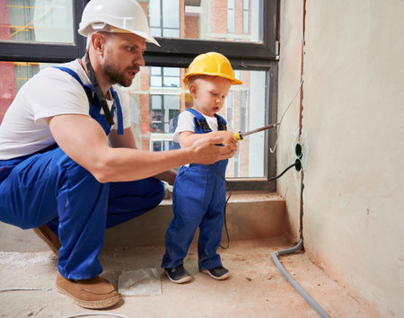 Male worker and little boy using welding repair tool while installing electric cables and sockets in apartment. Man and child with electric soldering iron working on home renovation.の写真素材