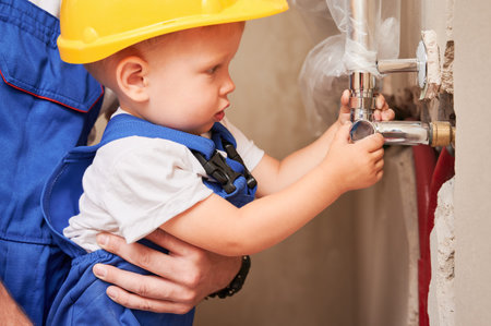Close up of father holding little son while child installing plumbing pipes in apartment under renovation. Man and kid in safety helmet working on installation of sanitary equipment at home.の写真素材