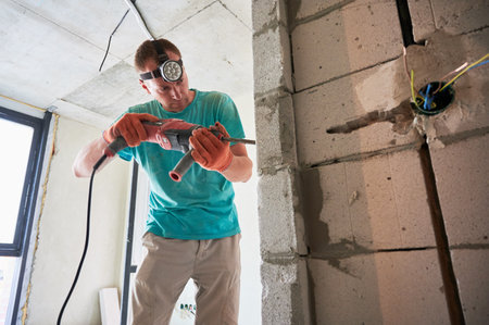 Male construction worker drilling brick wall with electric drill in apartment under renovation. Man...