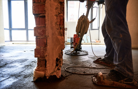 Close up view worker using troweling machine while screeding floor in apartment under renovation. Man finishing concrete surface with floor screed grinder machine in room with large windows.の写真素材