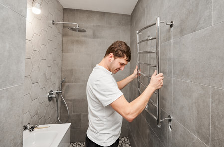 Plumber hanging electric heated towel rack on the wall in bathroom. Man installing stainless steel bath towel heater in apartment under renovation. Home renovation concept.の写真素材