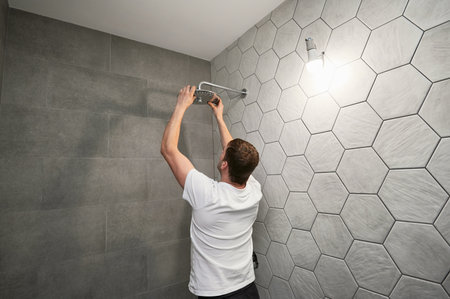 Male worker fixing bathroom showerhead while working on bathroom renovation. Back view of man plumber installing high pressure bath showerhead at home.の写真素材
