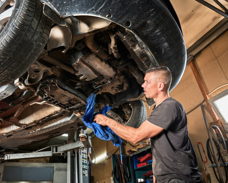 Repairman, worker repairing car, holding rag, wiping. Strong, hardworking man working in servicing center, mainteining automobiles. Concept of manual labor.の写真素材