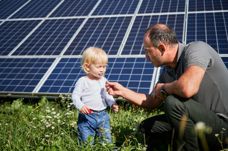 Young father showing his small child white flower in background of solar panels. Modern dad teaching his son love and care about nature. Concept of saving environment.の写真素材