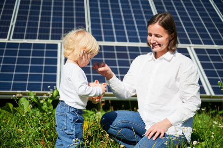 Little kid and his mom saving and putting money into ceramic piggy bank on background of solar panels. Mother teaching little child how to invest money in fututre.の写真素材