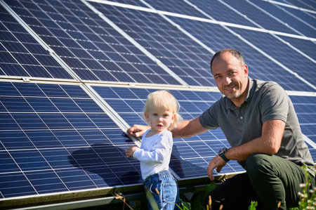 Portrait of man his small son next solar panels during sunny day. Modern father and cute child looking and smiling to camera. Little steps to alternative energy.の写真素材