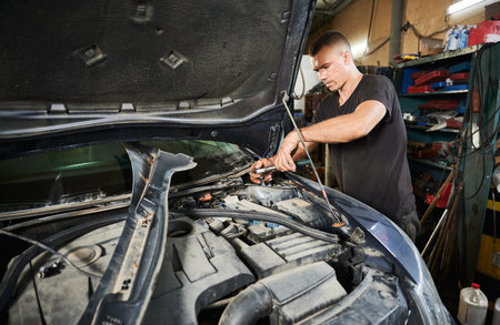 Concentrated, strong man opening hood of car, fixing engine. Professional worker, repairman holding screwdriver, repairing problem. Concept of manual labor.の写真素材