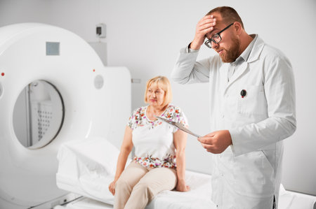 Medical computed tomography or MRI scanner. Shocked, surprised doctor looking at scan, examining results of MRI. Female patient sitting on couch on blurred background. Concept of healthcare.の写真素材