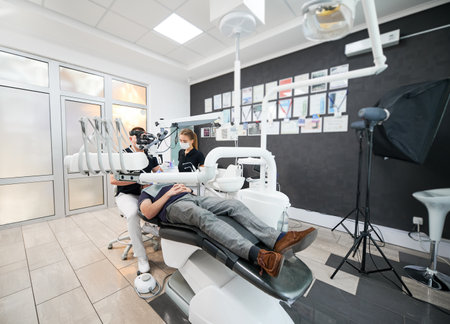 Dentists, working in clinic, examining, inspecting problem. Male doctor sitting on chair, looking in microscope, fixing teeth. Concept of healthcare and stomatology.の写真素材