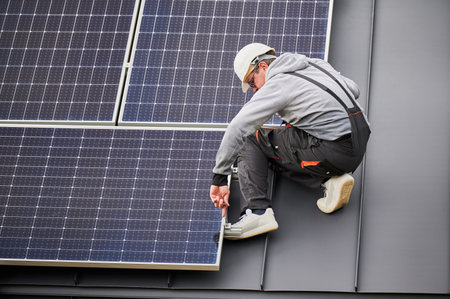 Man technician mounting photovoltaic solar panels on roof of house. Engineer in helmet installing solar module system with help of hex key. Concept of alternative, renewable energy.の写真素材