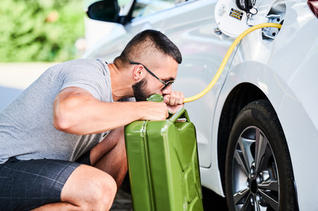 Weird man pumping gasoline from a gas tank into canister. Self-confident thief stealing fuel in broad daylight. Male adult trying to pump fuel from tank by hose.の写真素材