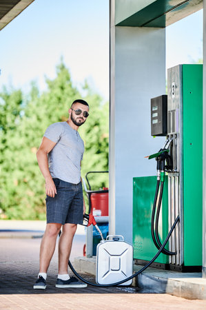 Portrait of young driver filling canister with gasoline. Man refueling canister with fuel in case of unforeseen circumstances. Male adult with gasoline pump refueling cistern.の写真素材