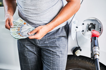 Man counting how much money he spending on fuel. Rising fuel prices concept. Close up view of male counting dollars on background refueling car.の写真素材