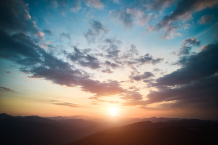 Panoramic view of bright evening sun and dramatic cloudy sky over mountains. Magnificent scenery of mountain hills under colorful evening sky with clouds and setting sun. Beauty of nature concept.の写真素材