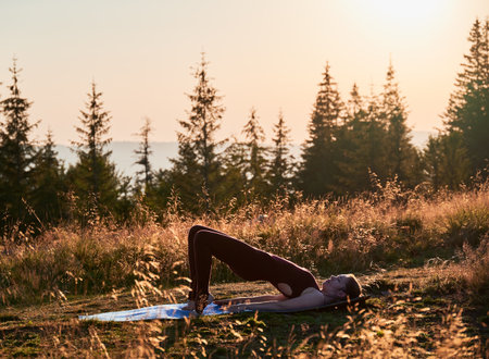 Pretty woman doing one leg bridge pose. Outdoors workout at early morning. Exercising on fresh air.の写真素材