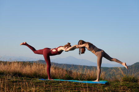 Two girls doing yoga pose at early morning. Sporty mother and her daughter exercising outside. Outdoor meditation in mountains.の写真素材
