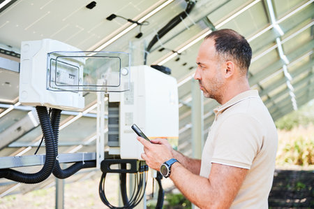 Configuring of photovoltaic solar battery. Man turning on switches. Young male looking at electric switchboard on back side of solar panel.の写真素材