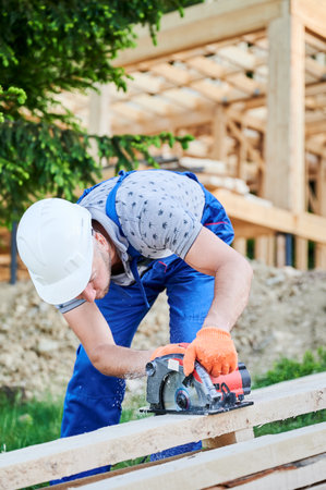Carpenter using circular saw for cutting wooden plank. Man worker building wooden frame house. The ideology behind modern, environmentally-conscious construction.の写真素材