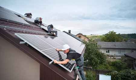 Men technicians mounting photovoltaic solar moduls on roof of house. Workmen in helmets installing...