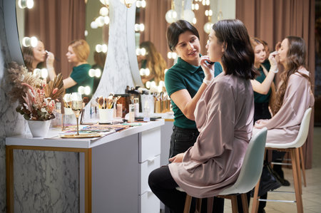 Professional makeup artist doing makeup for client in visage studio. Female beauty specialist using blending sponge while applying foundation on woman face.の写真素材