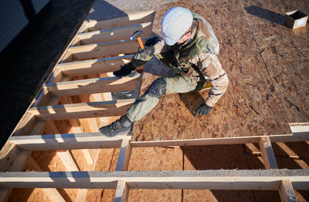 Carpenter hammering nail into OSB panel on the roof top of future cottage. Man worker building...