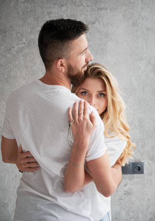 Woman holding house keys, embracing husband in new apartment and looking to the camera. Happy couple hugging and celebrating real estate purchase. Concept of love, new home and property purchase.の写真素材