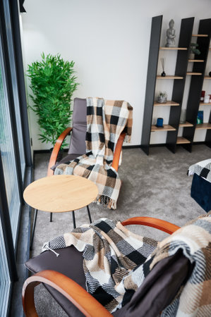 Modern living room with coffee table and armchairs for resting indoor. Side view of comfortable chairs with checkered plaids and small table standing near window in cozy room. Concept of comfort.の写真素材