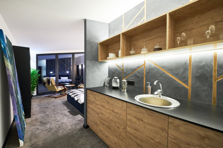 Open plan kitchen area and living room in modern, cozy house. Side view of contemporary wooden kitchen counter looking through to resting area and panoramic window on background. Concept of interior.の写真素材