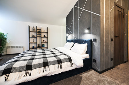 Light, simply furnished bedroom with big bed and decorated wooden shelves indoors. Side view of wide bed, with checkered plaid against gray wall with geometric pattern in bedroom. Concept of interior.の写真素材