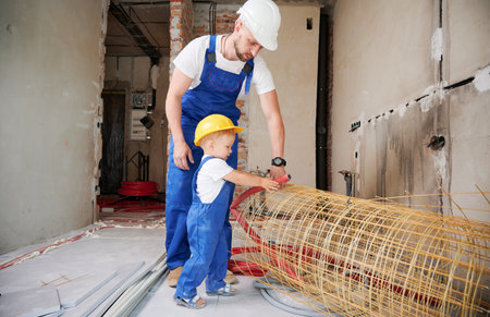 Father and little son working with mesh fiberglass rebar and pipes in apartment under renovation. Male builder and kid in work overalls using construction materials at home.の写真素材