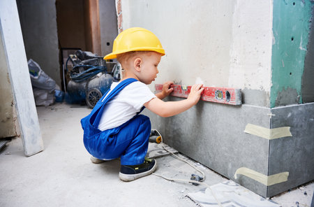 Little boy construction worker measuring wall surface with spirit level tool. Kid in work overalls using bubble level instrument while preparing wall for repair works at home during renovation.の写真素材