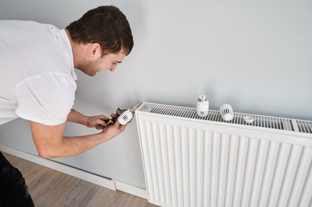 Male plumber using construction pliers tool while installing heating system in new apartment. Man mounting household heating radiator on the wall. Home renovation concept.の写真素材