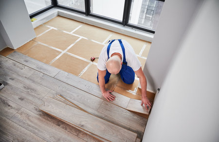 Top view of man construction worker installing laminate wooden flooring in living room. Man laying laminate wood plank on floor underlayment in new flat. Home renovation concept.の写真素材