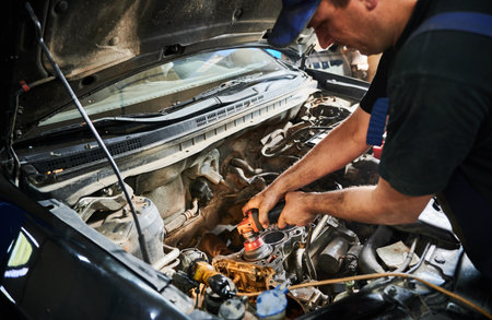 Close up of worker, repairman, mechanic wearing cap and uniform, repairing car. Strong, hardworking male working in garage, auto, servicing center. Concept of repairing car.の写真素材