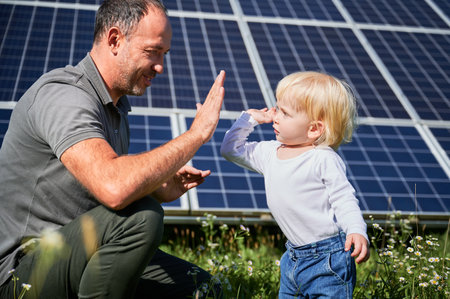 Smiling father and his little child giving each other high-five on background of solar panels. Young father enjoy spending time with his son. Happy family of two on background of solar panels.の写真素材